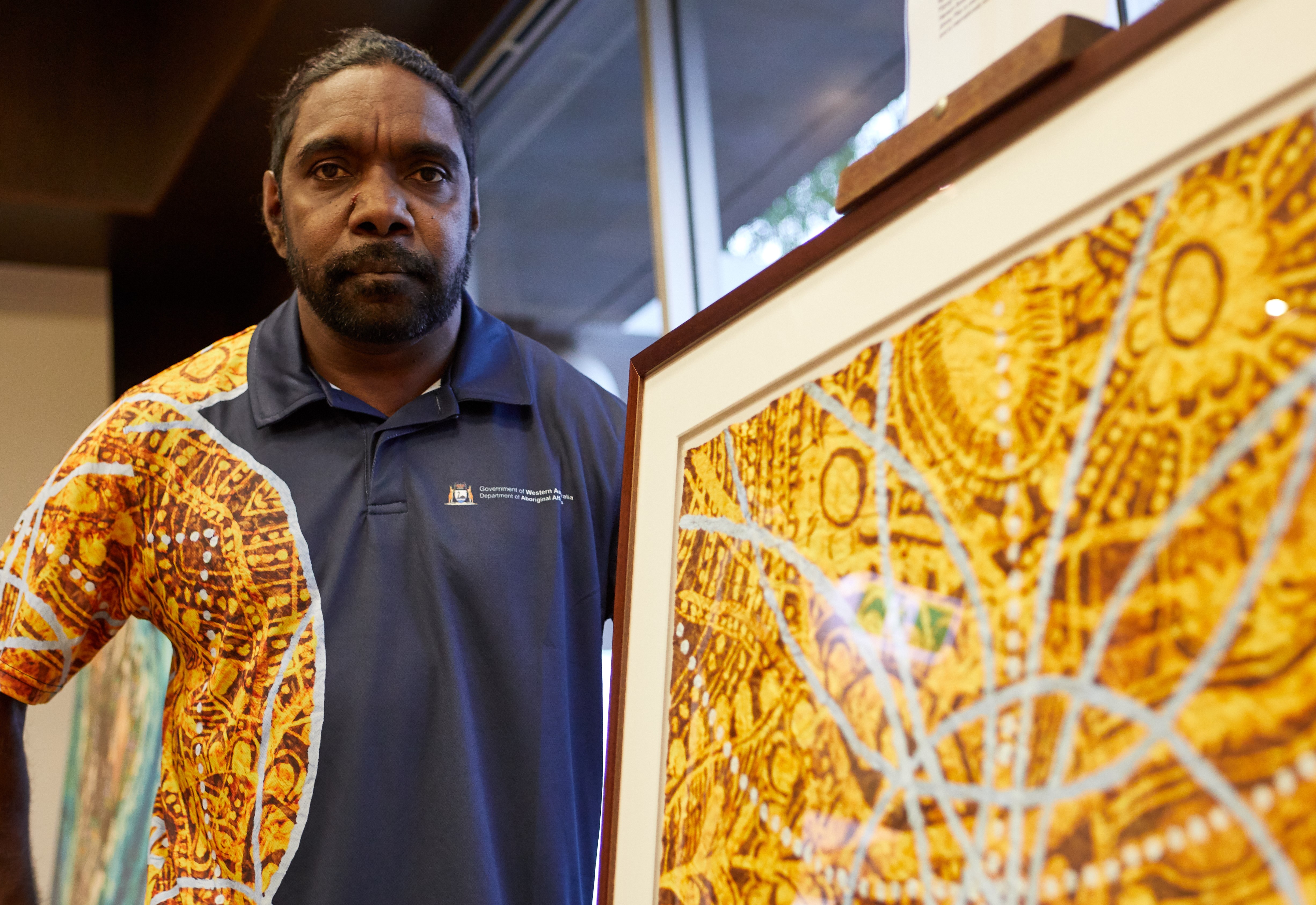 A man posing next to a framed colourful artwork