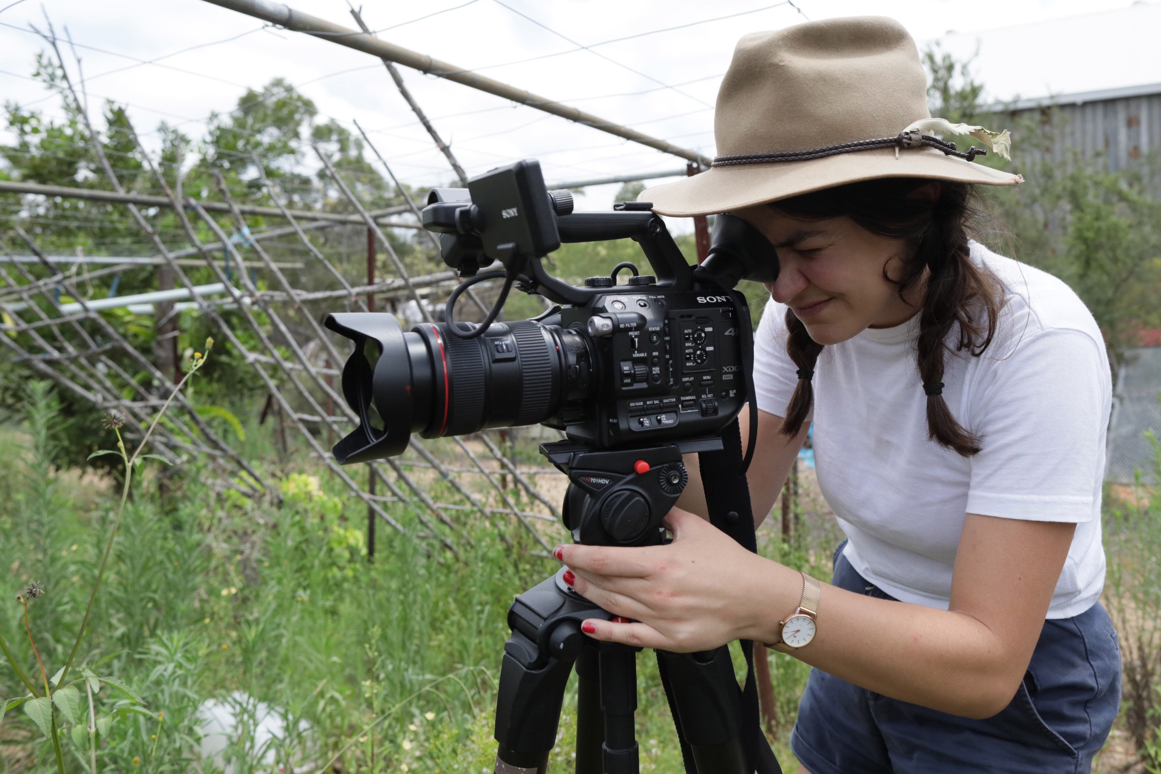 A young woman with her head tilted forward looking into the viewer of a movie camera on a tripid.