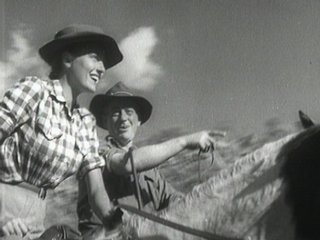 Film still of a woman and a man on horseback. The man points into the distance