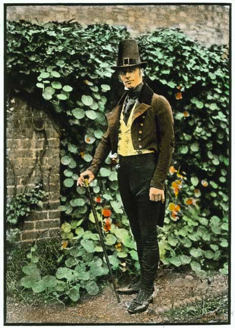 A man stands in front of a garden wall covered in leaves. He