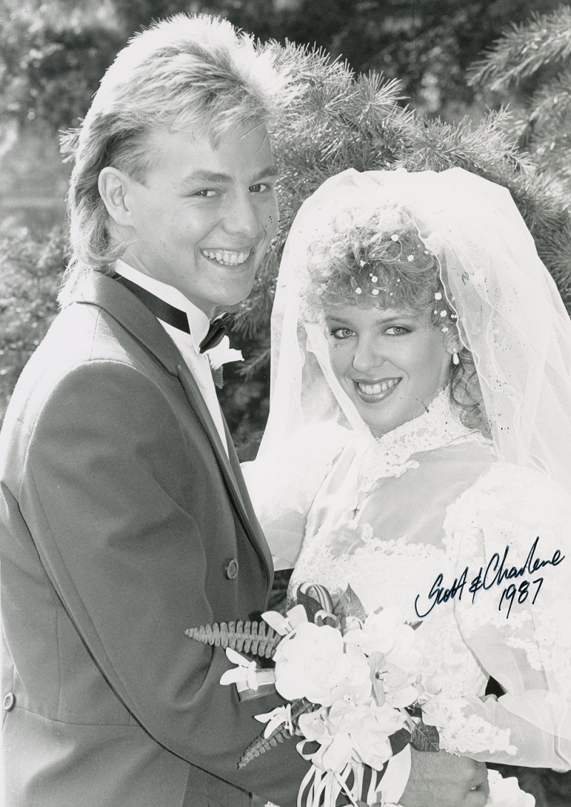 Scott and Charlene played by Jason Donovan and Kylie Minogue are all smiles on their wedding day. Charlene holds a bouquet of flowers. Handwritten text reads 