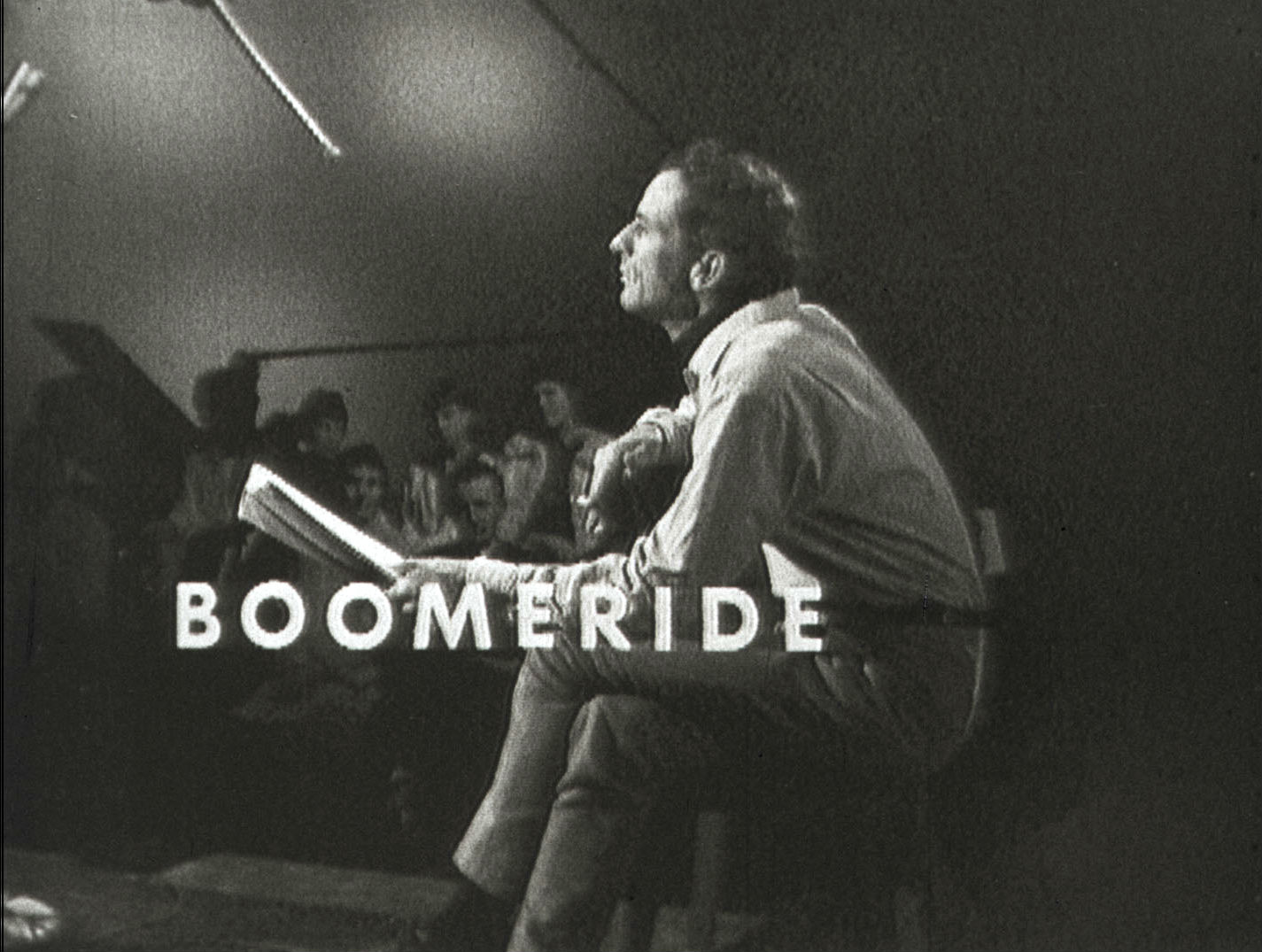 Australian singer/songwriter Charles Marawood pictured in profile sitting on a stool with legs crossed and playing a guitar. In the background there are some members of a live TV studio audience. The title 