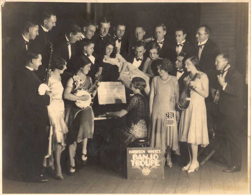 A group of people holding banjos and standing around a piano.