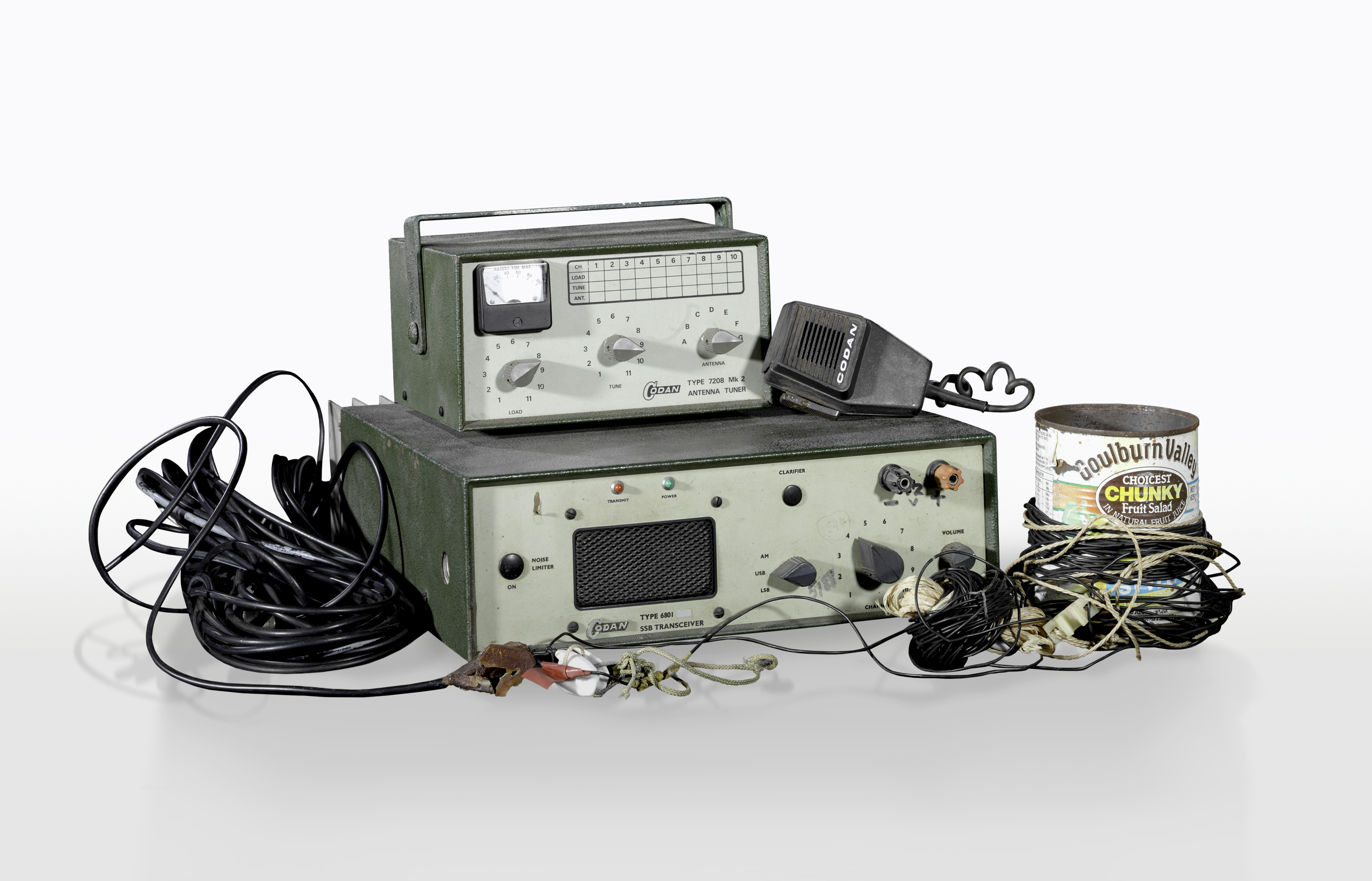 A collection of homemade radio equipment including a transceiver box with knobs and speaker, an antenna tuner, cords and a fruit salad tin used as an antenna.