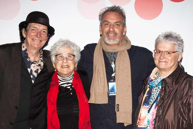 Four people standing in front of a media wall at a film premiere and smiling at the camera.