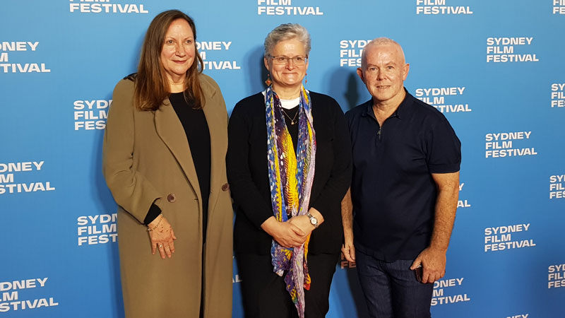 Two women and a man standing in front of a media wall.