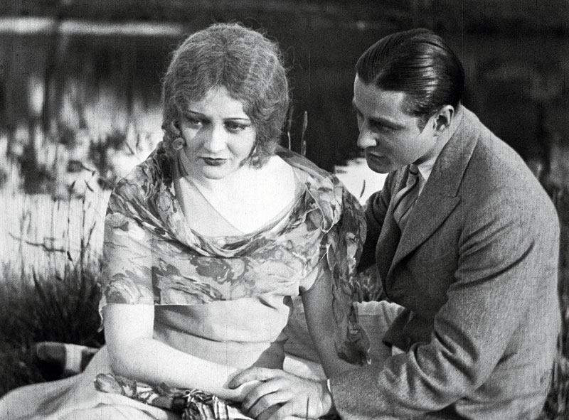 A young woman and man holding hands and looking forlorn in a scene from silent film The Cheaters.