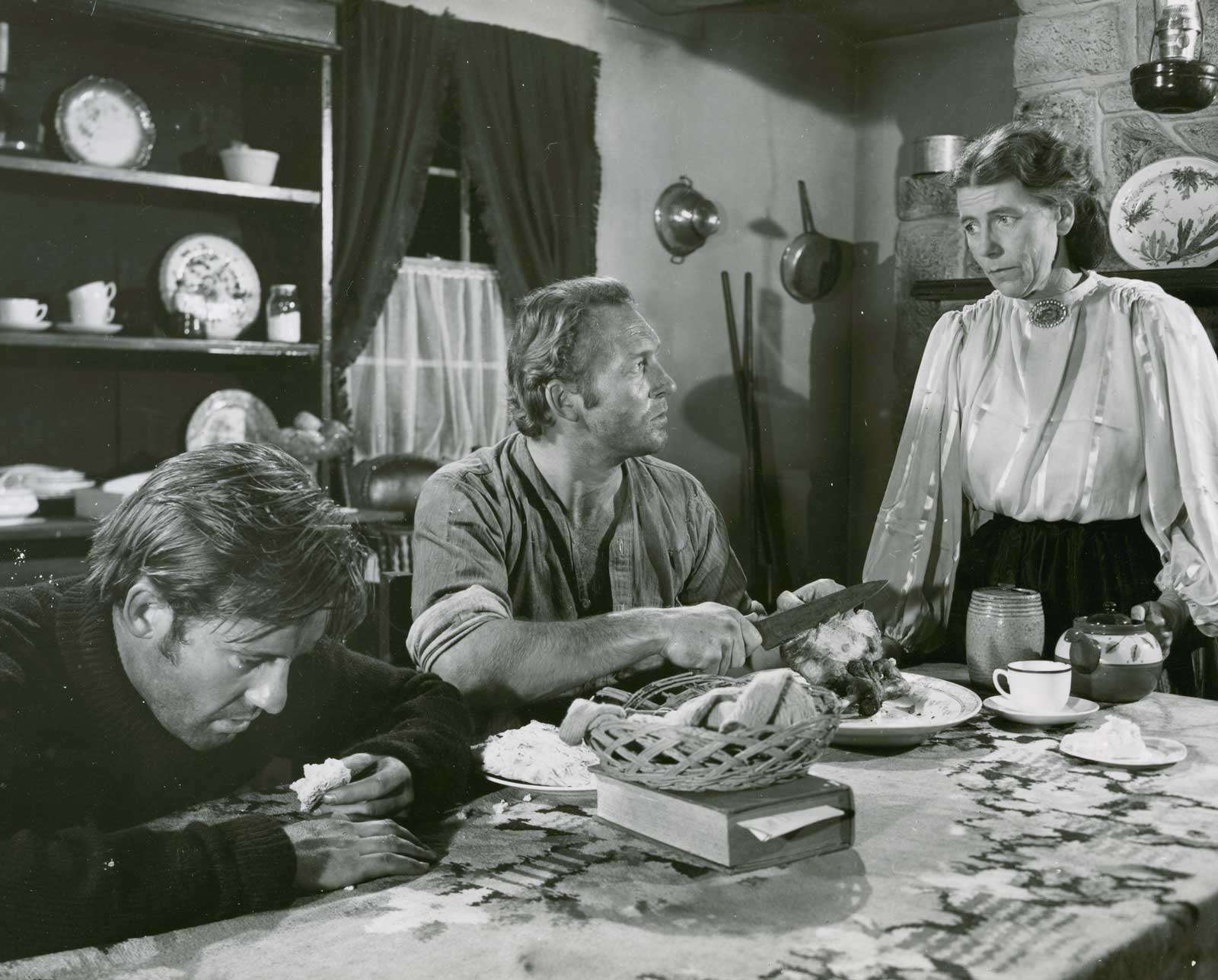 Two tired looking men seated at a table talking to a woman who is standing looking at them