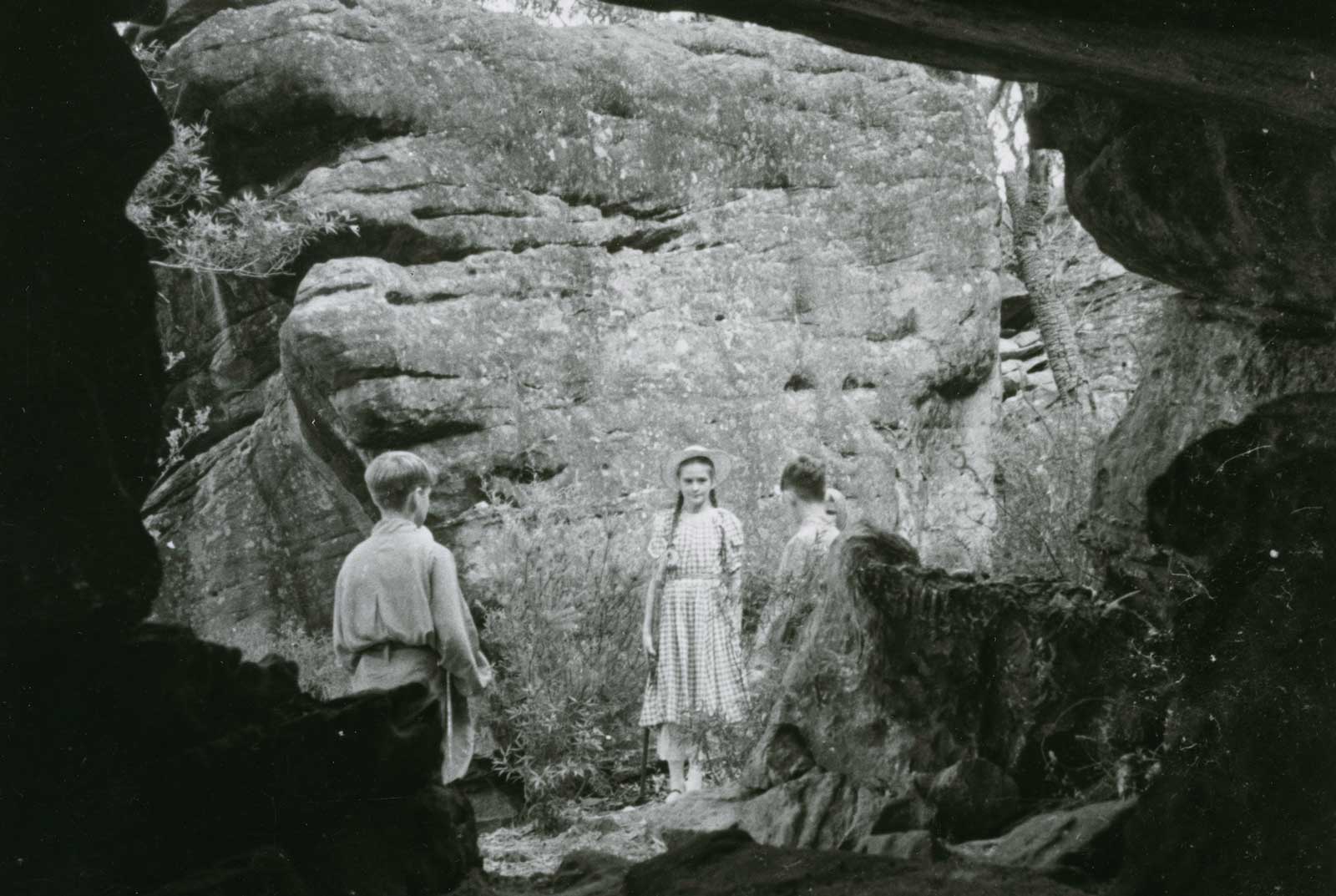 Three children standing in front of a cliff outside a cave
