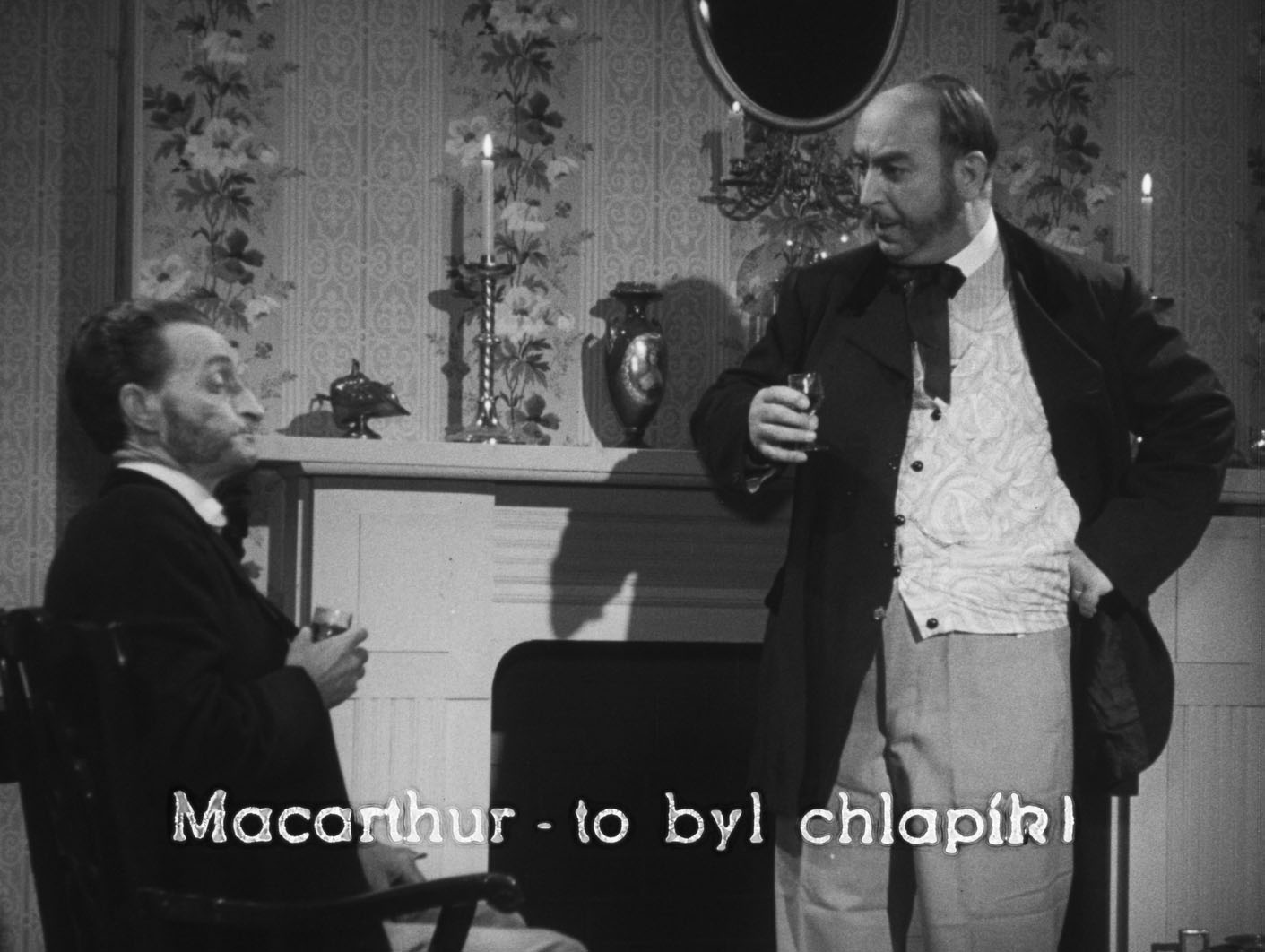 Two gentlemen in 19th century attire standing in front of a fireplace holding drinks