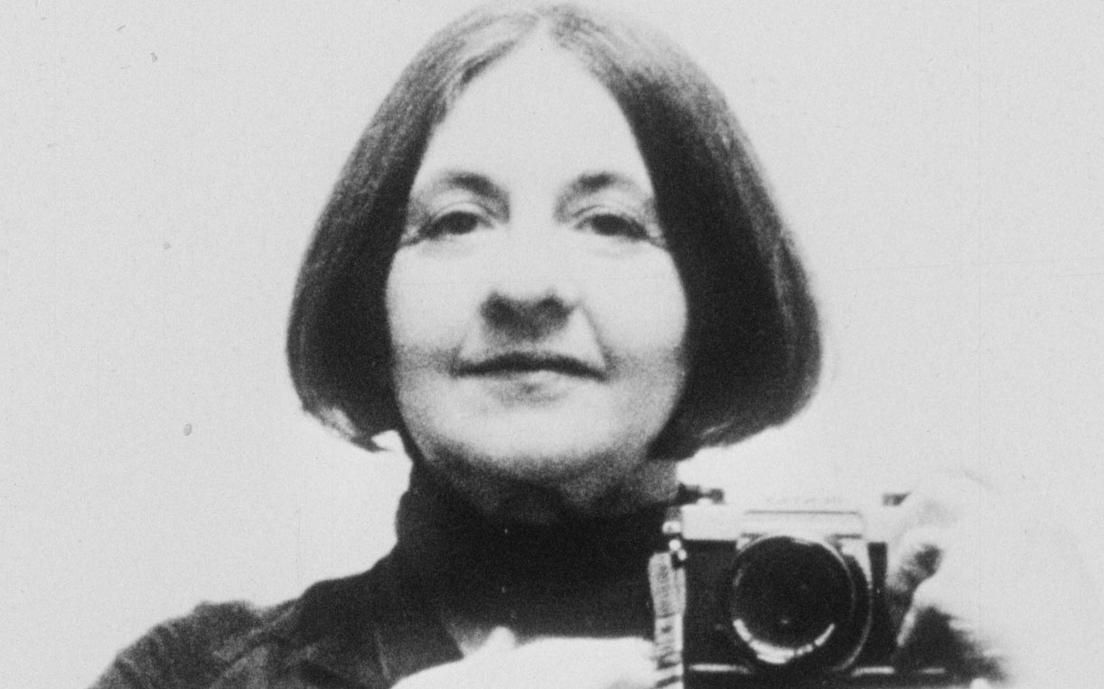 Experimental filmmaker Corinne Cantrill holding up an analogue film camera and smiling