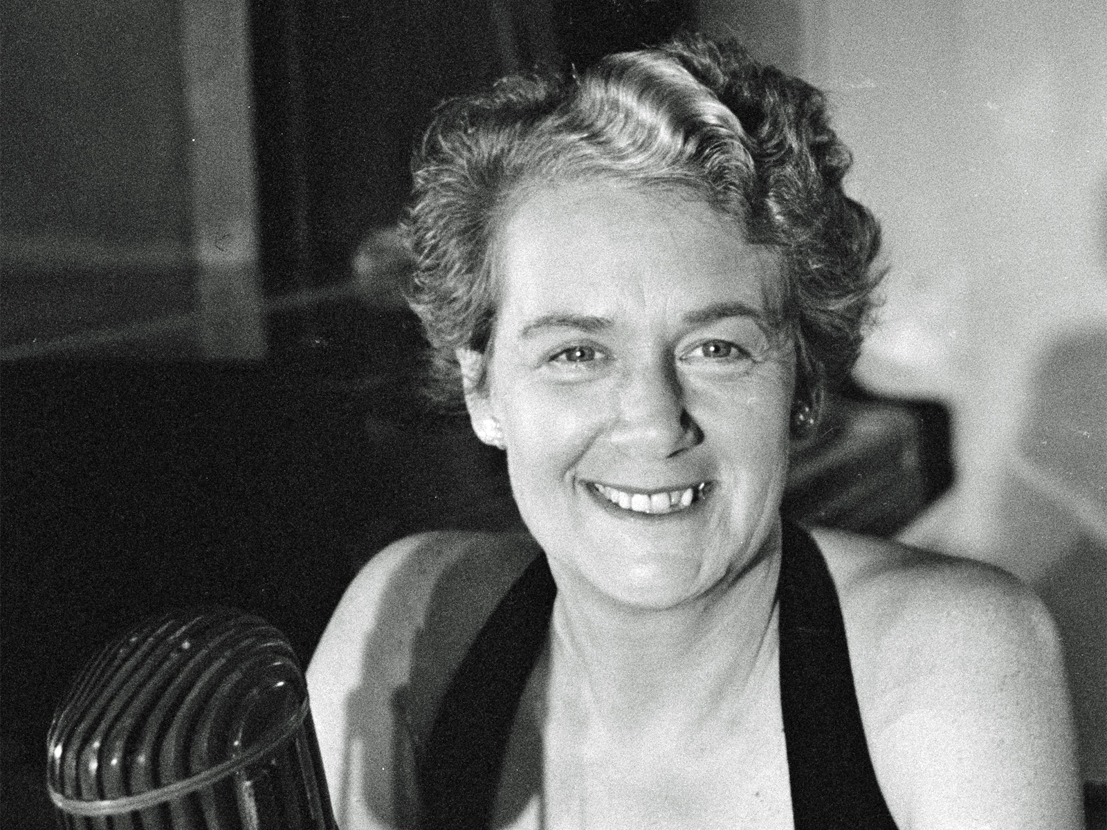Head and shoulders shot of a woman smiling at camera with a radio mic in front of her.