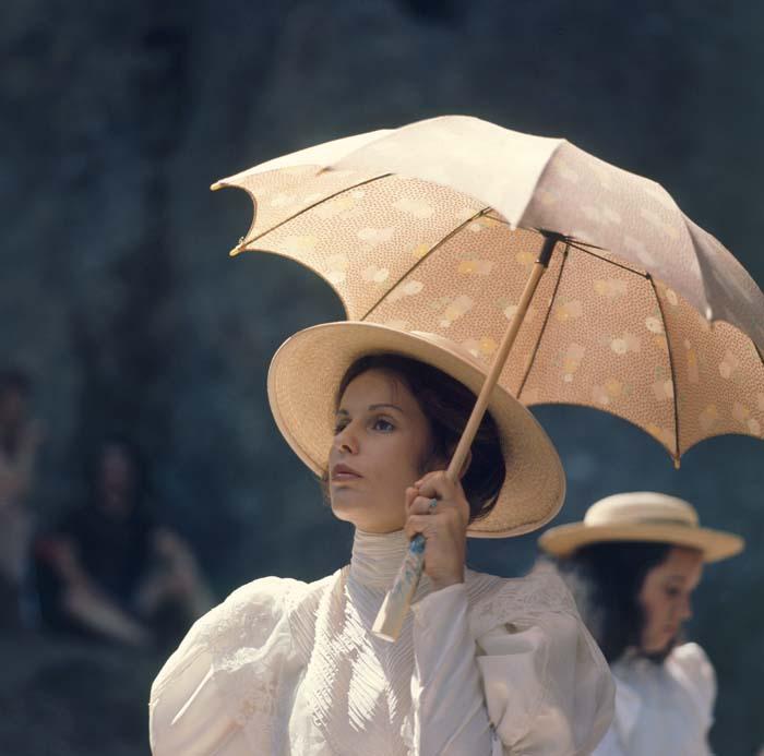 Helen Morse as the French mistress, in a white dress and holding a parasol, at Hanging Rock in a scene from Picnic at Hanging Rock