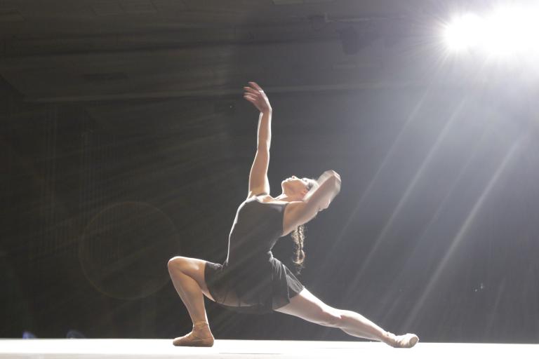 A dancer in a black dress poses on stage under a bright light A dancer in a black dress poses on stage under a bright light