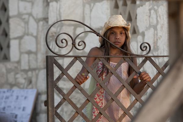 A young girl wearing a hat looking over an iron gate A young girl wearing a hat looking over an iron gate