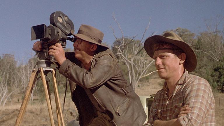 Bill Hunter looks through the viewfinder of a newsreel camera on location with his assistant, played by Chris Haywood, in the film Newsfront.