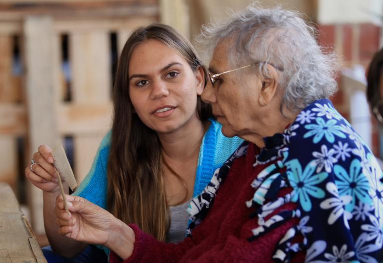 A young and elder woman are sitting at a table holding and looking at a photograph A young and elder woman are sitting at a table holding and looking at a photograph