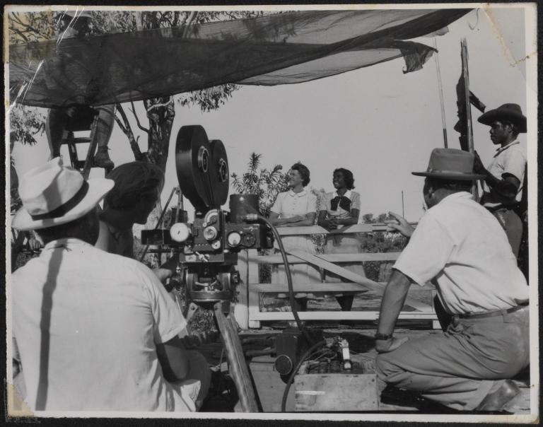 Scene from a movie being filmed showing camera crew in foreground and actors in the background