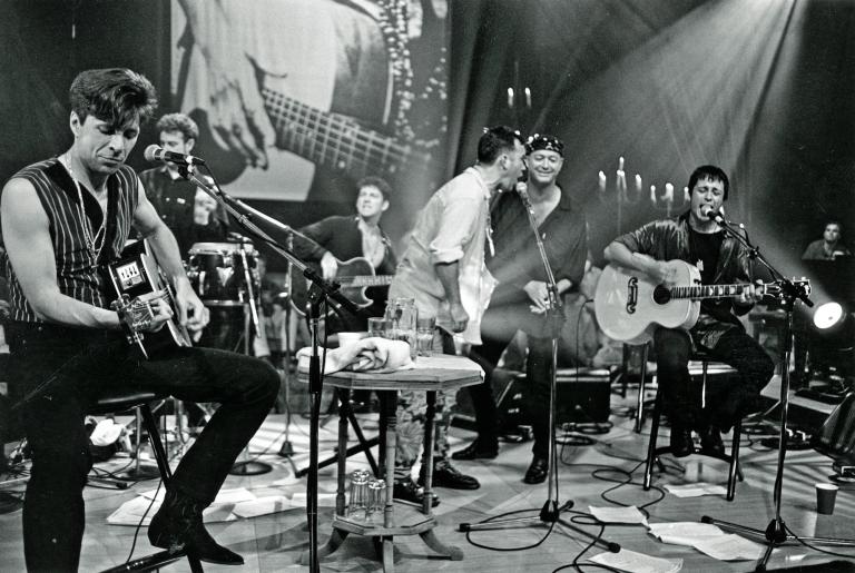 Jimmy Barnes on stage singing into a microphone standing next to Vince Lovegrove. Diesel is sitting playing guitar to their right. On the left is another guitarist.