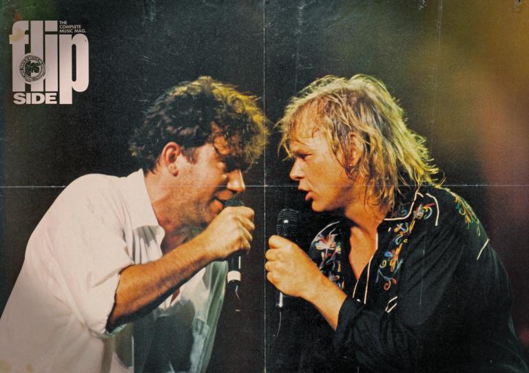 Jimmy Barnes and John Farnham Head and shoulders image of Jimmy Barnes and John Farnham facing eachc other with microphones in their hands. Jimmy Barnes is dressed in a white shirt and John Farnham in a black embroidered shirt. Title of the magazine in white text at top.