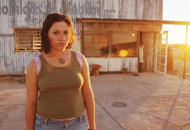 A woman wearing a backpack at sunset standing in front of a congregated iron building