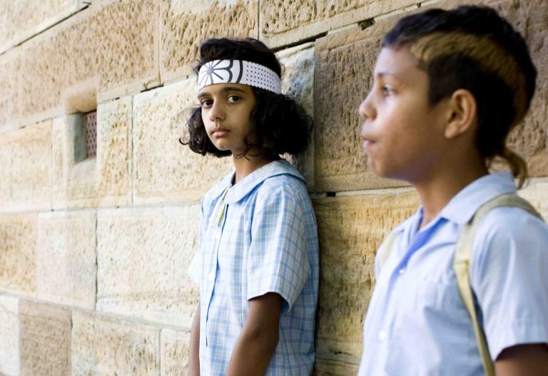 Two children in school uniform standing with their backs against a wall
