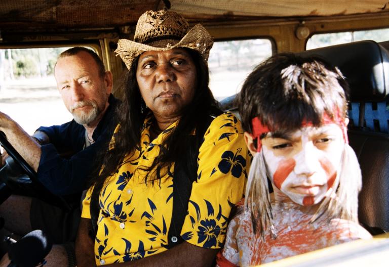 A man, woman and child with painted face and body sit in the front of a car