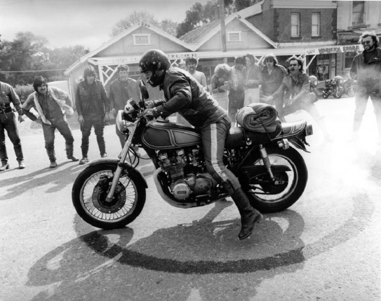 Motorcycle burnout in a country street while others look on.