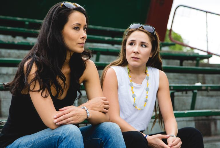 Two young women sitting in the stands of a local sporting ground.