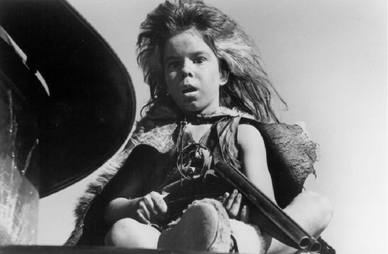 Wild looking child on a truck holding a shotgun.