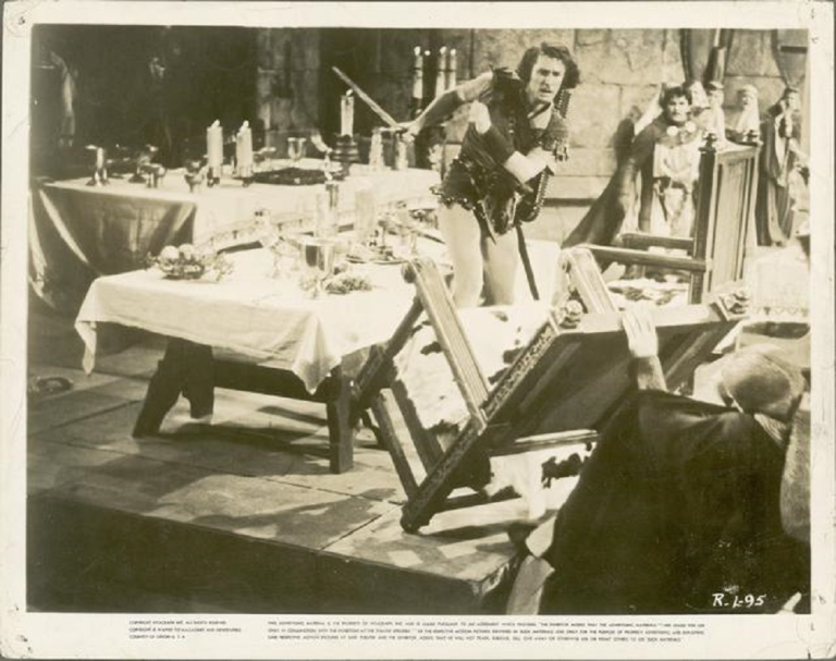 Errol Flynn upturns a table in a baqueting hall.
