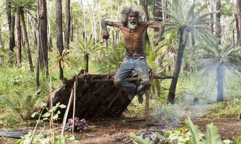 Charlie's Country - David Gulpilil jumping up An older David Gulpilil jumping up in the air in the bush. He's in front of a lean-to shelter.