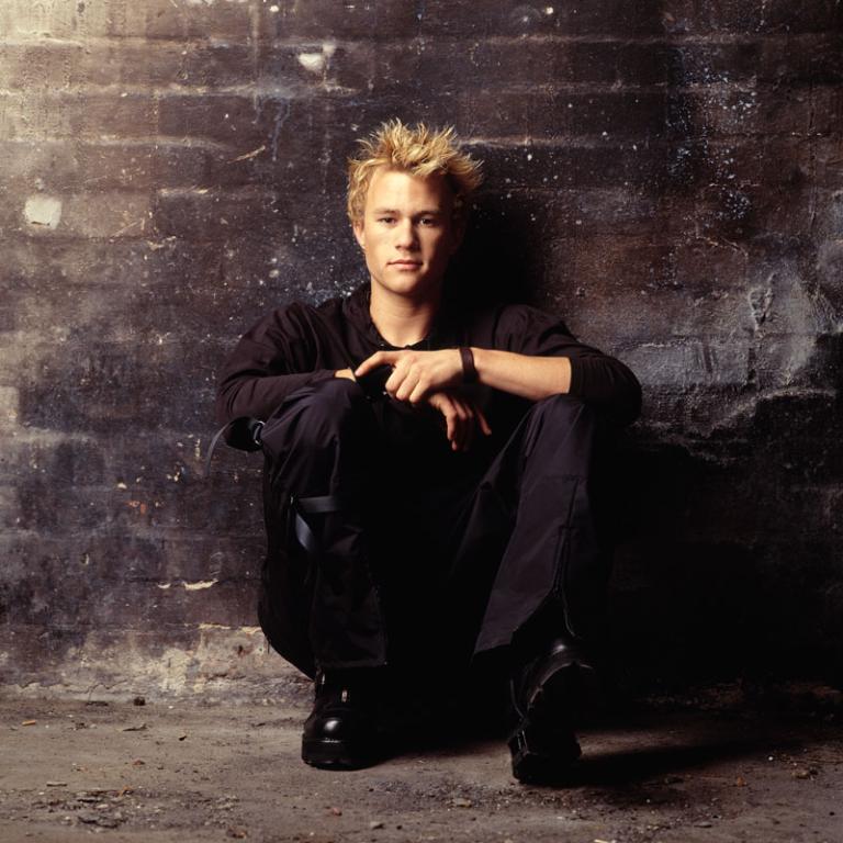 Heath Ledger at Jacksue Gallery, Perth Heath Ledger crouches up against a wall looking at the camera.