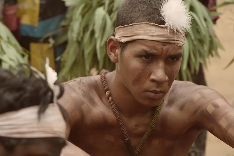 A head and shoulders shot of an Indigenous teenager wearing traditional headwear and body paint.