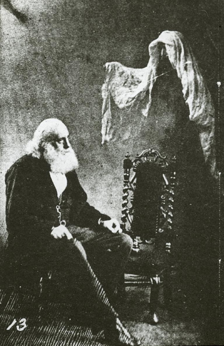 Spirit glass slide by Frederick Hudson Glass sldie of an old, bearded man setaed with a ghost hovering to his left with its arm extended