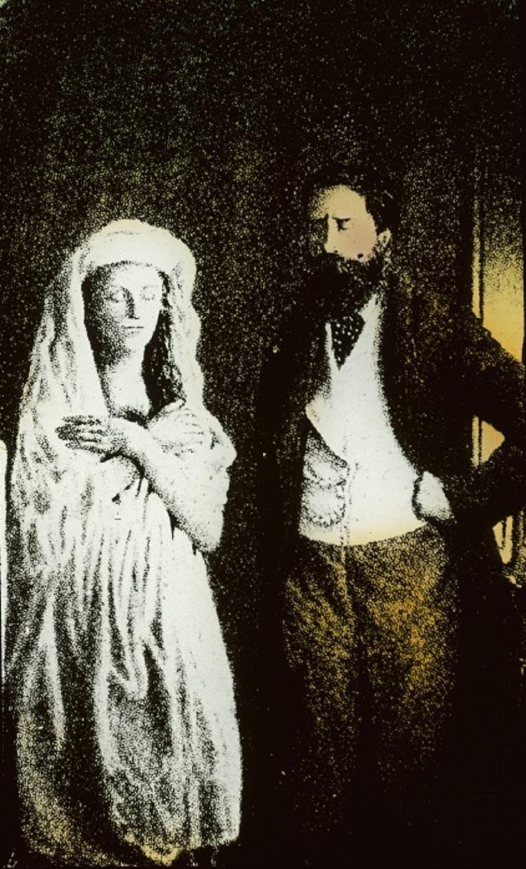 Sir William Crookes with the spirit, Katie King Colour glass slide showing a man standing with hands on his hips, looking at a spirit in a white robe with hands crossed over her chest.