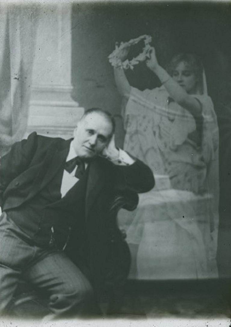 Spirit crowning a man with a wreath Black and white glass slide showing a man sitting on a chair resting his left arm over the side, a spirit hovering at his left holding a wreath over him.