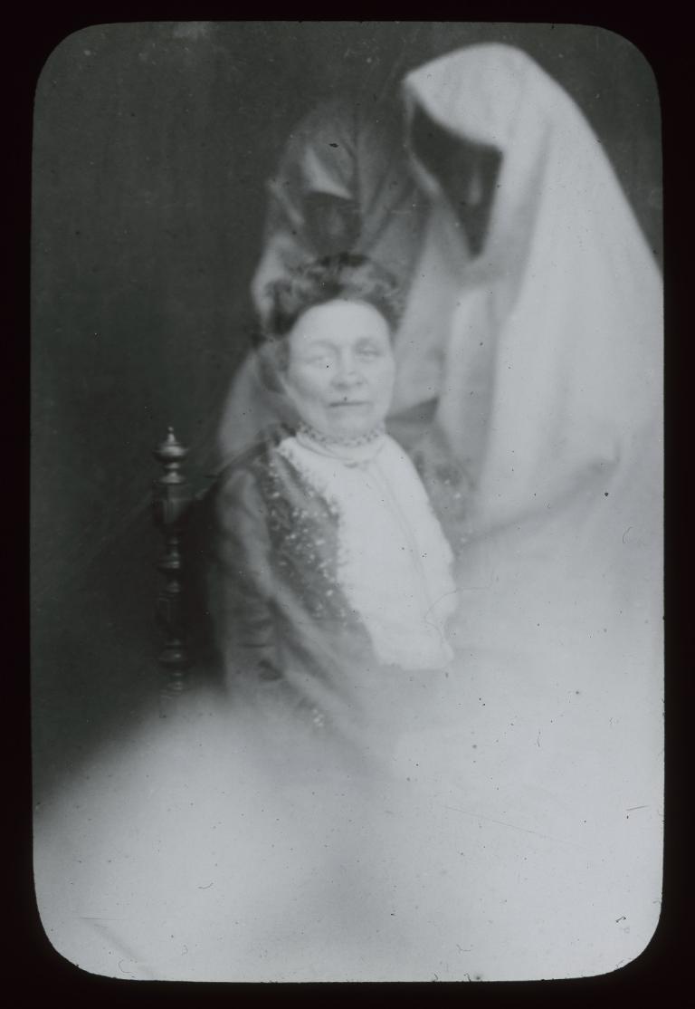 Glass slide with two spirits Black and white glass slide showing two spirits, one behind and one to the left of a woman sitting on a chair