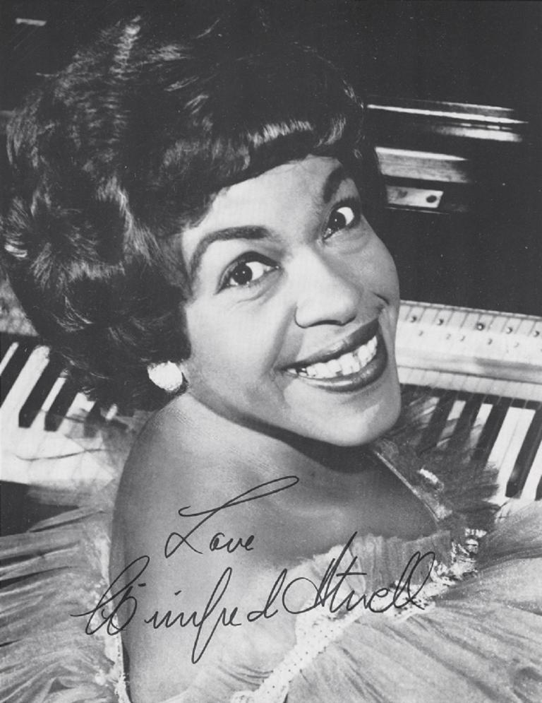 Autographed photo of Winifred Atwell sitting at the piano look up at the camera