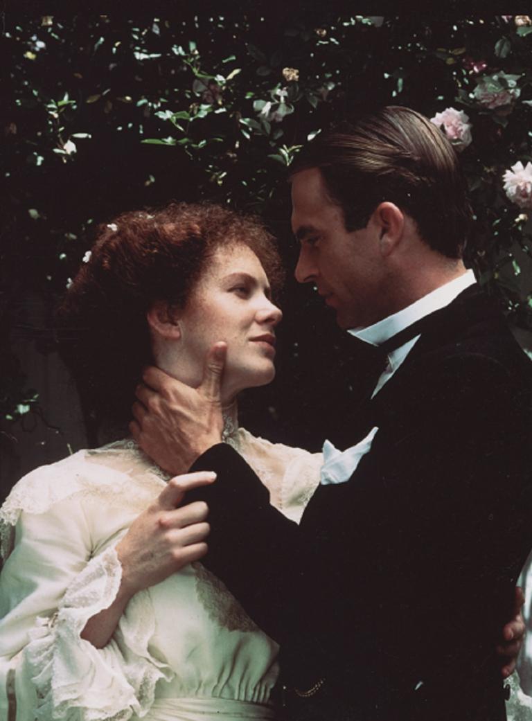 A man and a woman in period costume look lovingly into each others eyes in an outdoor setting