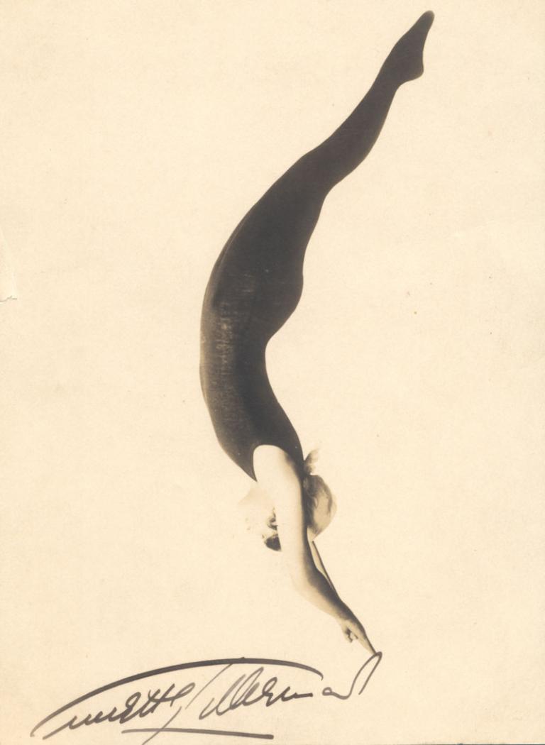 A signed publicity still of Annette Kellerman. She is wearing a figure-hugging swim suit and appears to be diving with her hands pointed downwards. She is on a white background.