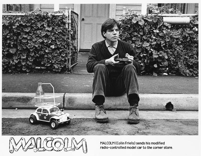Malcolm sits on the curb sending his remote controlled car to the corner shop for milk