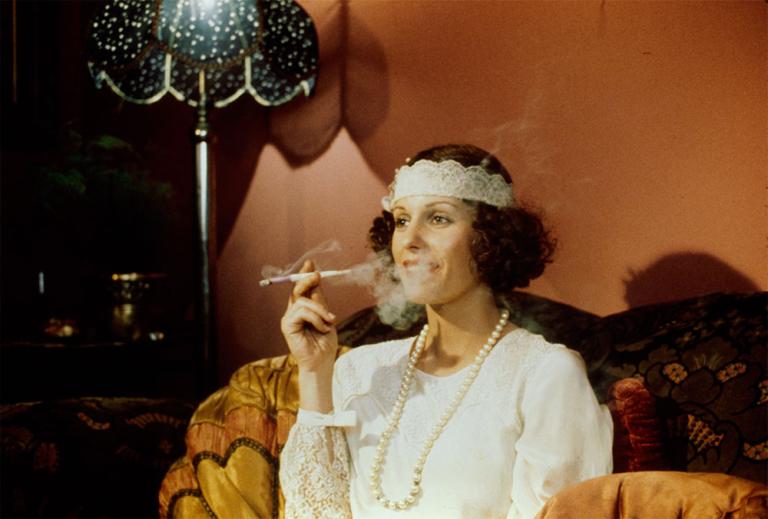 Helen Morse as Caddie dressed as a flapper Film still of Helen Morse as Caddie dressed as a flapper, seated and smoking using a long stemmed cigarette holder.