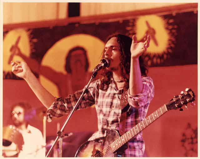 Musician with guitar singing into a microphone.