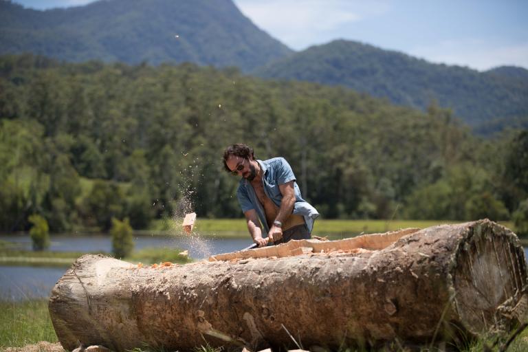 A man shapes a large tree trunk with an axe.