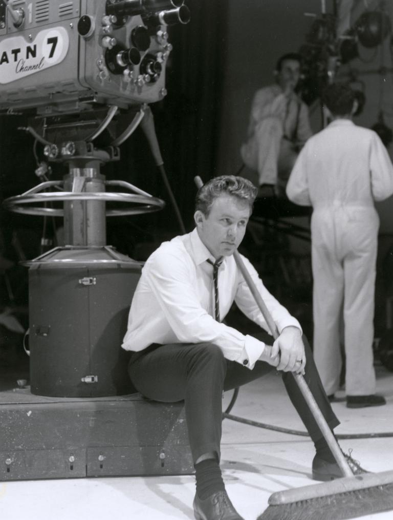 Johnny O'Keefe with broom on the set of 'Sing Sing Sing' Johnny O'Keefe sitting at the base of a camera holding a broom on the set of 'Sing Sing Sing'