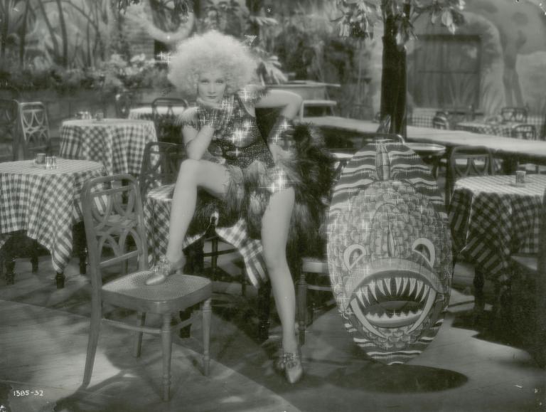 Marlene Dietrich sits on a table in a cafe looking at the camera in a still from the film Blonde Venus, 1932.