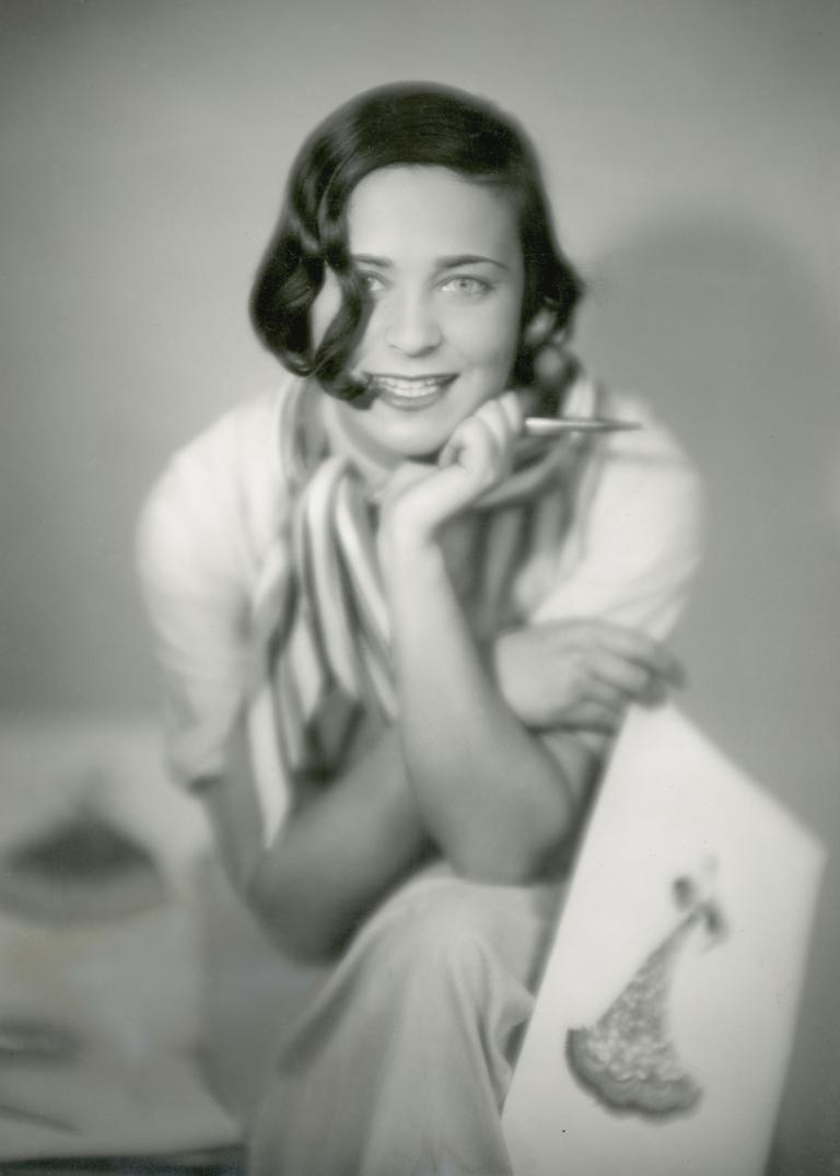 Designer Gerdago holds a costume sketch and gazes into the camera, 1930.