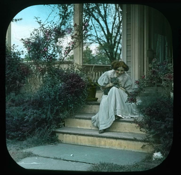 Eileen My Own cinema slide Young woman sitting on some steps in front of a house and holding a grey cat, circa 1906.