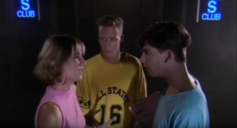 Zoe Carides and Ben Mendelhson stare at each other at the entrance of a night club. There are blue neon signs reading 'S Club' on both sides of the door. Paul Gleeson stands behind them.
